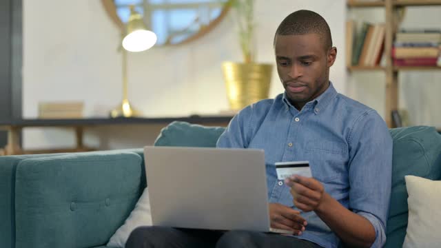 沙发上的非洲青年在笔记本电脑上成功网购视频素材