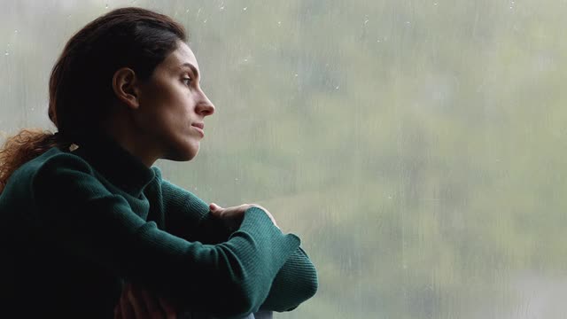 阴天里，孤独的女人坐在室内的窗台上视频素材
