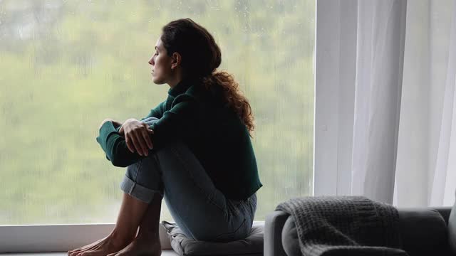 孤独的女性坐在窗台上看外面下雨的天气视频素材