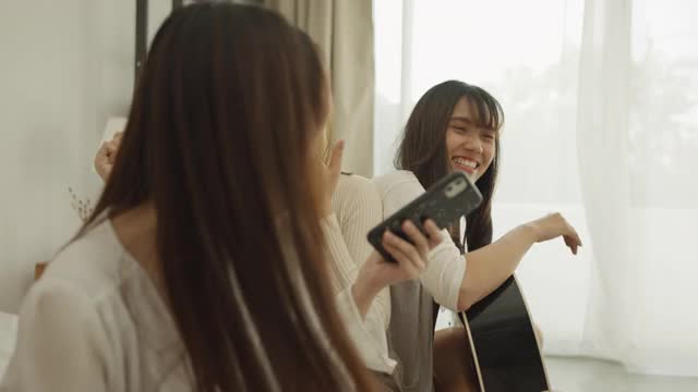 女孩和她的朋友在卧室的床上弹吉他视频素材