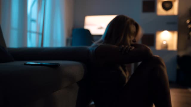 抑郁的女人晚上坐在地板上，手机放在沙发上视频下载