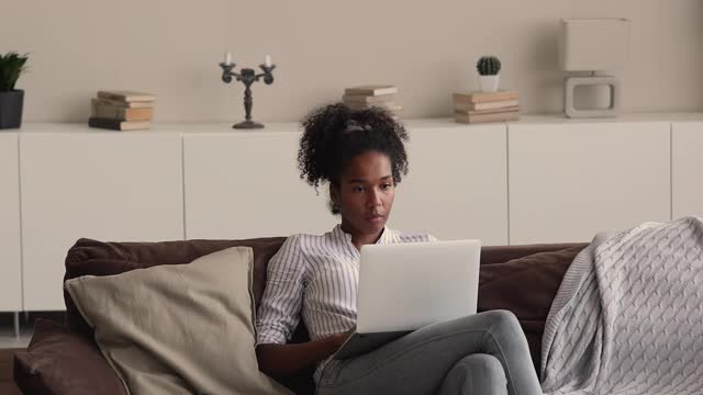 年轻漂亮的非洲女人坐在沙发上用笔记本电脑休息视频素材