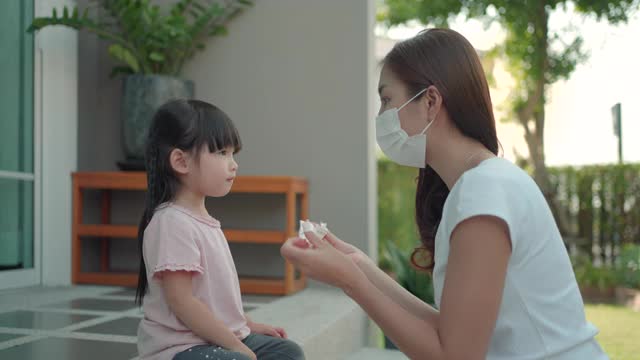 亚洲母亲在女儿上学前帮助女儿戴上防护口罩，保护新冠肺炎疫情。准备好学校的概念。视频下载