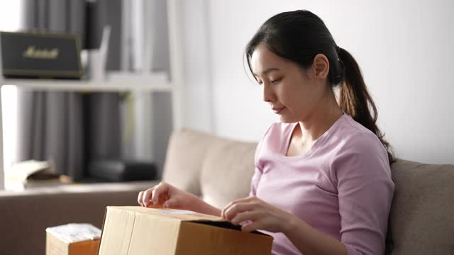 兴奋的年轻亚洲女顾客在家里打开包裹盒子视频下载