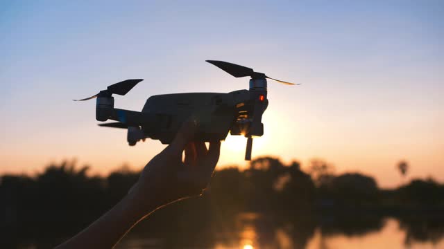 人手启动无人机起飞，在夕阳的背景下飞向天空。视频下载