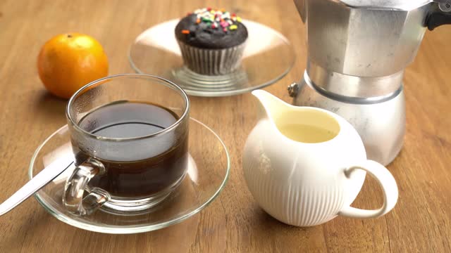 将新鲜牛奶倒入玻璃杯中的黑咖啡中，放在木桌上，配上成熟的橘子和巧克力松饼视频下载
