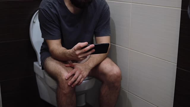 坐在马桶上的男人用手机用智能手机年轻的拉丁男人视频素材