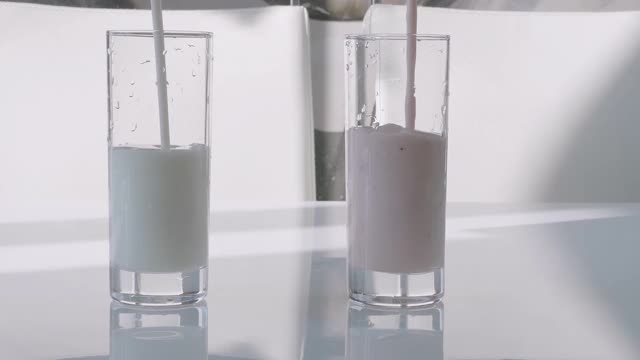将新鲜乳制品倒入玻璃杯中，草莓水果酸奶在玻璃杯中，特写。倒酸乳酒视频素材