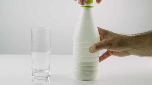 从一个白色背景的玻璃杯的塑料瓶中倒入牛奶，乳制品，酸奶在玻璃杯中。视频素材