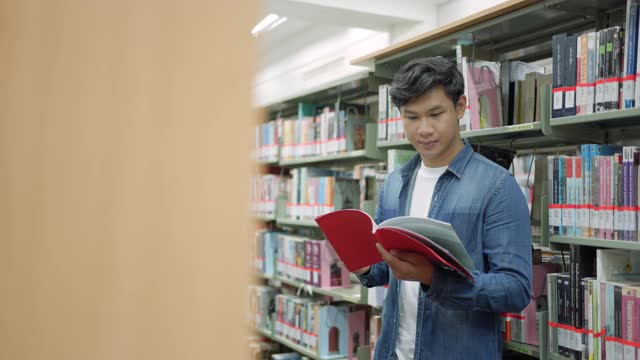 聪明的亚洲人大学学生阅读之间的书架与校园图书馆的copyspace。视频素材