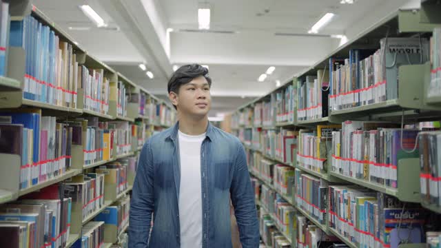 聪明的亚洲人大学学生阅读之间的书架与校园图书馆的copyspace。视频素材