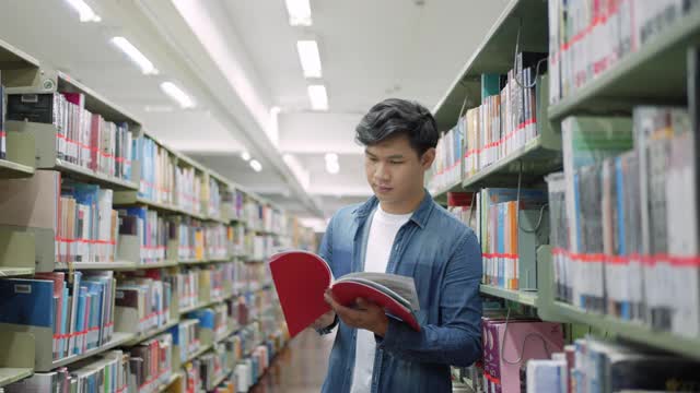 聪明的亚洲人大学学生阅读之间的书架与校园图书馆的copyspace。视频下载