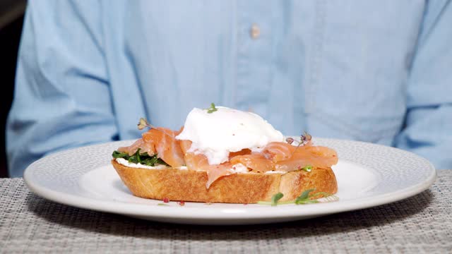 特写美味的三明治与鲑鱼和水煮鸡蛋在一个白色的盘子。厨师在给客人上菜前用手套将酱汁倒在意式烤面包上视频素材