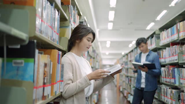 聪明的亚洲男女大学生读书之间的书架与校园图书馆的拷贝空间。视频下载