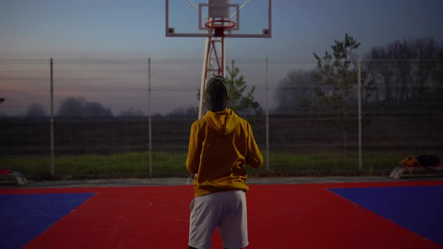 一个十几岁的男孩在户外运动场上打篮球视频素材
