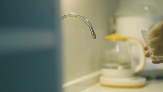 一个女人从厨房水槽的水龙头里倒了一杯干净的水到一个干净的杯子里视频素材