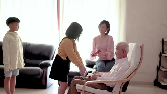 亚洲华人爷爷在家给孙子孙女发红包。快乐带着笑脸。视频素材