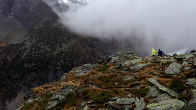 无人机拍摄的两名跑步者跑上一座俯瞰山谷的山的边缘视频下载