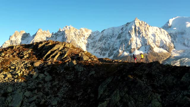 无人机拍摄的两个跑步者沿着山的边缘跑，在山顶停下来视频下载