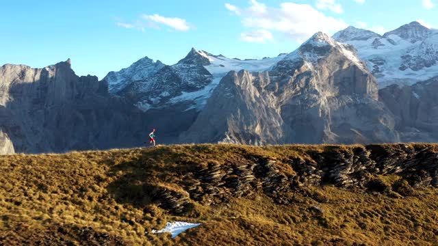无人机拍摄的一个跑步者沿着山的边缘跑，后面是山视频下载