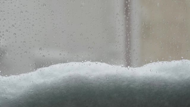 一扇窗户上的雨滴和飘落的雪花视频素材