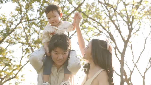 年轻的爸爸和妈妈抱着快乐的小男孩在空中，年轻的爸爸在公园里玩视频素材