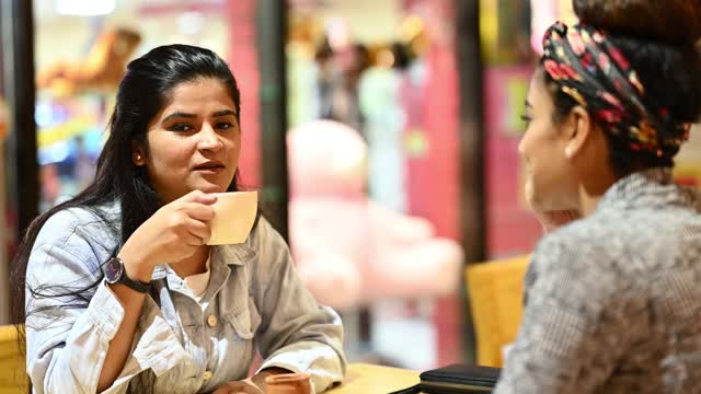 两个年轻的女商人一边工作或学习，一边坐在咖啡馆里互相聊天。视频素材