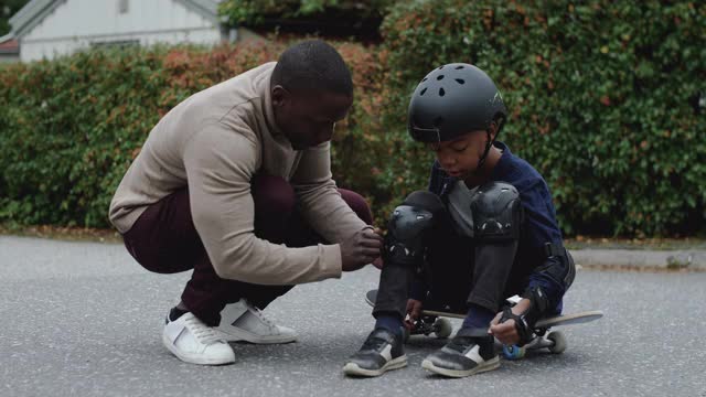 手持拍摄的父亲协助儿子与安全齿轮滑板视频素材
