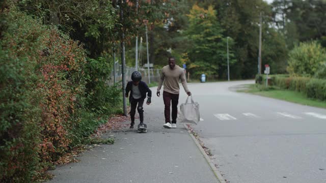 手持拍摄的男子携带可重复使用的袋子，而儿子滑板在人行道上的植物视频素材
