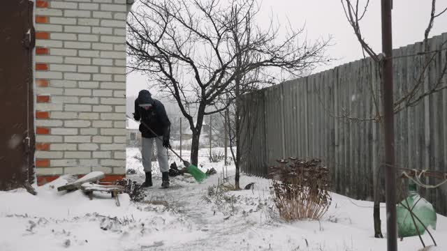 一名男子在暴风雪中清扫后院的积雪。降雪。男性用扫帚扫雪视频素材