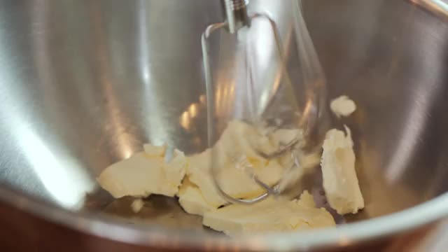 特写黄油被打/打在一个不锈钢碗在一个木制的背景桌子。视频素材