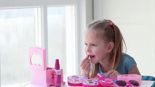 美丽的小女孩用儿童唇膏涂上嘴唇，照镜子。孩子们在家玩玩具美容沙龙。视频素材