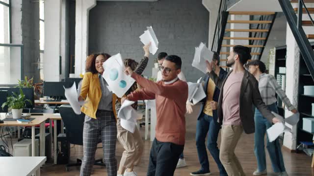 快乐的员工在现代开放式办公室里跳舞、扔文件，享受派对视频素材