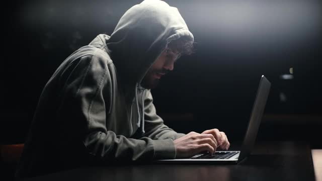 侧视图，年轻的大胡子程序员在黑房间的书桌上黑客网站或密码。视频素材