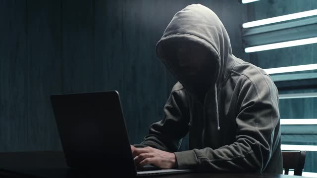 一名不知名的黑客穿着带兜帽的运动衫在笔记本电脑上输入密码。视频素材