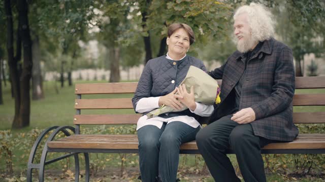 一对幸福恩爱的退休夫妇坐在秋天的公园里聊天。积极微笑的资深白种人男女户外约会。快乐的妻子和丈夫享受闲暇。爱和归属感。视频素材