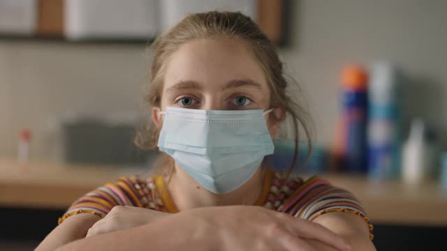 SLO MO CU一名女孩坐在医疗诊所里，摘下防护口罩的肖像视频下载