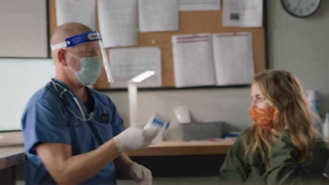 善良的医疗工作者在一个医疗诊所内测量年轻女子的体温视频下载
