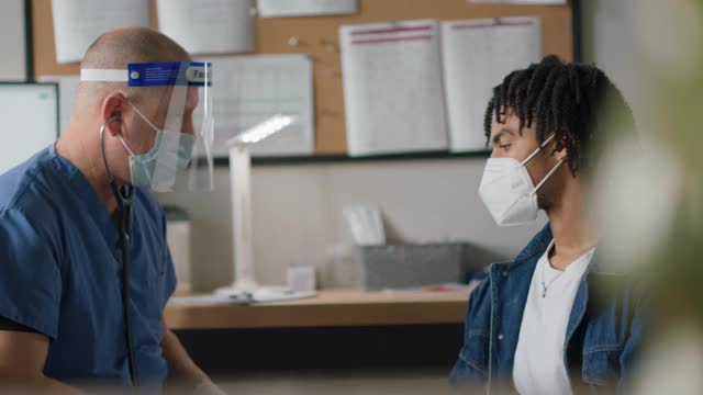 年轻男子在医疗诊所深呼吸，医疗保健专业人员使用听诊器听他的肺视频下载