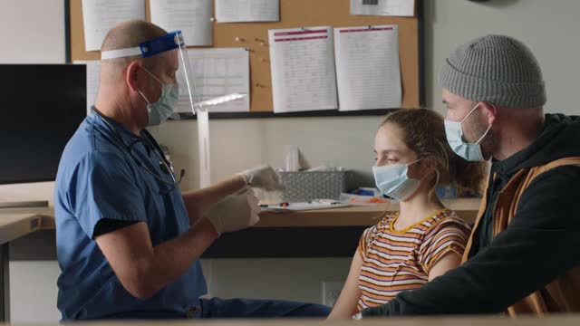 当医生给女儿接种COVID-19疫苗时，支持女儿的父亲握着女儿的手视频素材