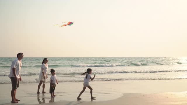 亚洲父母和两个孩子一起跑和玩风筝在海滩上日落视频素材
