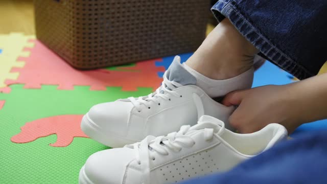 女孩坐在家里的地板上，穿着新的白色运动鞋。视频素材