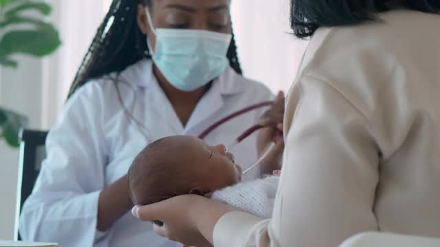 非洲裔女儿科医生在医院与母亲看病时，用听诊器听新生儿1个月大的心脏和与父母、婴儿病人交谈。医患会诊概念。视频下载