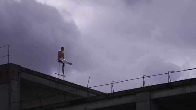 强大的马戏团艺术家保持平衡，一只手在屋顶的边缘对惊人的云景。风险、勇气和激情的概念视频下载