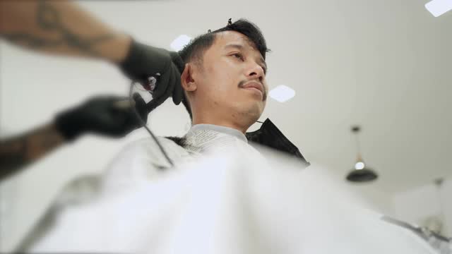 亚洲年轻男子剪头发时把面罩移到一边，预防传染病，新常态的生活方式。2019冠状病毒病大流行重新开放业务。低角度展示视频素材