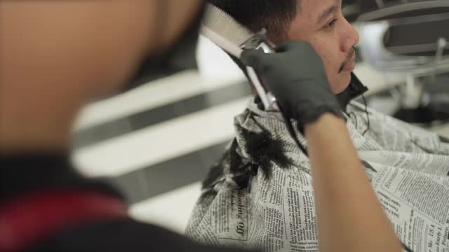一名亚洲年轻人在理发店剪头发，戴着黑色的防护面具，新常态的生活方式。视频素材