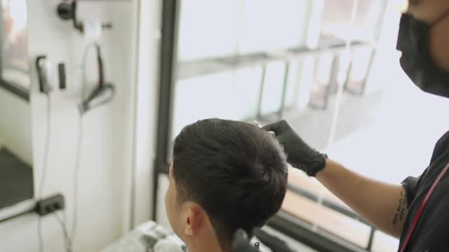 亚洲男性理发店，肩后理发师服务好，精心打扮，剃须刀，男理发师的老板戴着黑色手套口罩，以保护新冠肺炎大流行视频素材