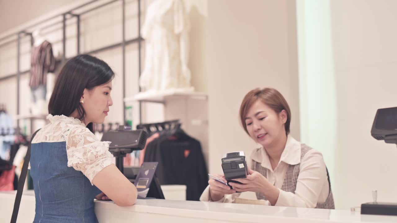 亚洲华人精品店女店主互动与她的客户收银员与信用卡购买结账视频素材
