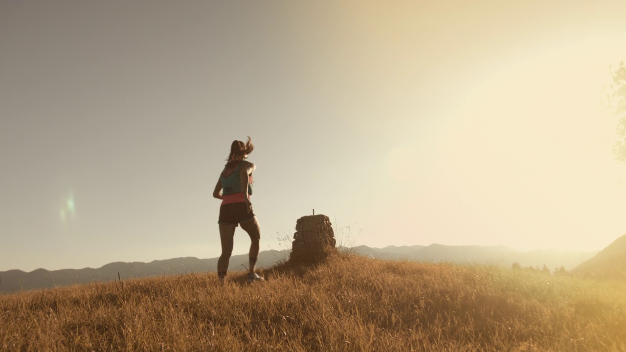健康的女人跑上山，爬上岩石山在金色的光- SLO MO视频下载
