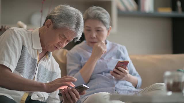 亚洲华人老年夫妇老花眼在周末闲暇时间试图在客厅学习使用智能手机有困难视频素材